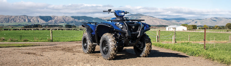 Yamaha 4x4 ATV parked on a farm road with a scenic farm background of grass paddocks and fields.