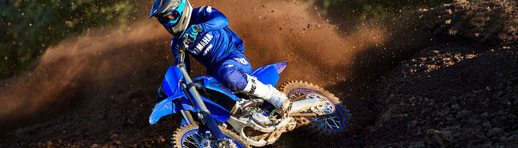 MX rider in branded Yamaha gear riding a Yamaha MX bike on a track berm and roosting dirt behind him.